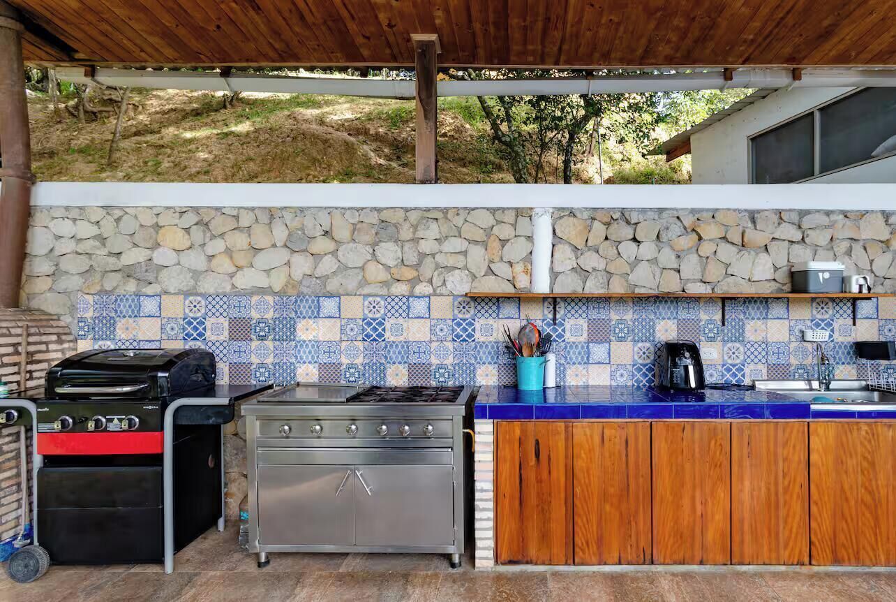 An outdoor kitchen with a stone backsplash, a gas stove, a grill, and a sink.