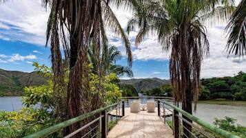 Uma ponte com guarda-corpo que leva a uma área de estar com vista para um corpo de água e colinas.