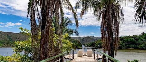 A bridge with a railing leading to a seating area overlooking a body of water and hills.