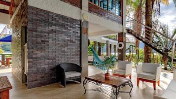 A spacious outdoor area with a brick wall, wicker furniture, a hammock, and a staircase leading to an upper level.