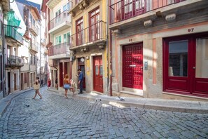 A cobblestone street lined with multi-story buildings, some with balconies and red doors. - Historic Porto Studio Steps from Clérigos Tower (Porto)