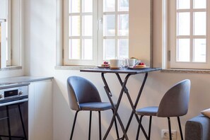 A kitchen area with a table and two chairs, a window with a view, and a stove. - Historic Porto Studio Steps from Clérigos Tower (Porto)