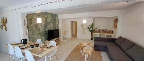 Una sala moderna con comedor, un sofá gris y una televisión.