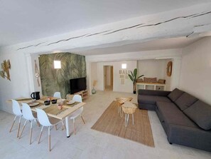 A modern living room with a dining area, a grey sofa, and a television. - The Balinese (Castres)