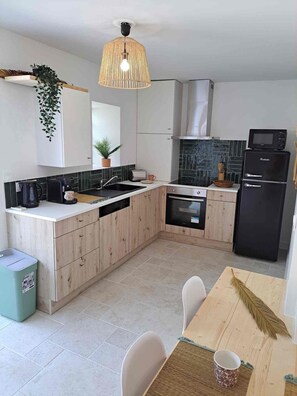 A modern kitchen with a central island, built-in appliances, and a hanging light fixture. - The Balinese (Castres)