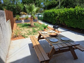 A wooden picnic table set outdoors with plates, cutlery, and a barbecue grill. - The Balinese (Castres)