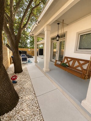 A covered outdoor patio with a wooden swing, a barbecue grill, and a seating area. - Fully Renovated Beach Retreat in Sunnyside (Panama City Beach)