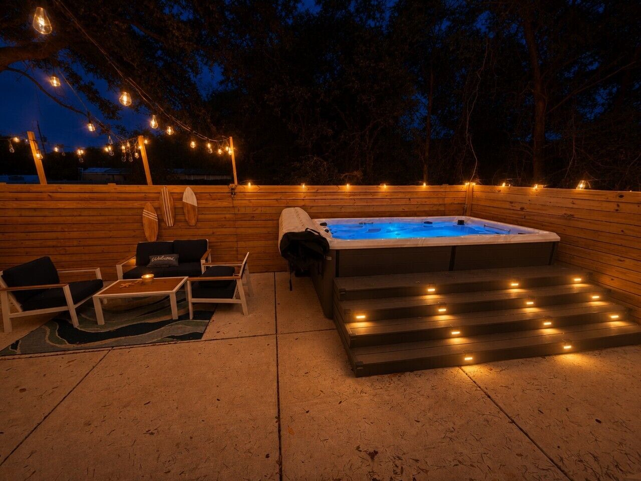 An outdoor hot tub area with steps leading up to it, surrounded by wooden walls and string lights.