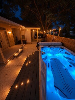 A hot tub with a wooden deck and string lights, surrounded by a covered patio area. - Sunnyside 3BR Retreat | Heated Swim Spa | Near 30A | Sleeps 9 (Panama City Beach)