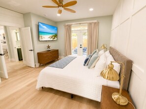 A bedroom with a bed, a television, a ceiling fan, and a view of the outdoors. - Sunnyside 3BR Retreat | Heated Swim Spa | Near 30A | Sleeps 9 (Panama City Beach)