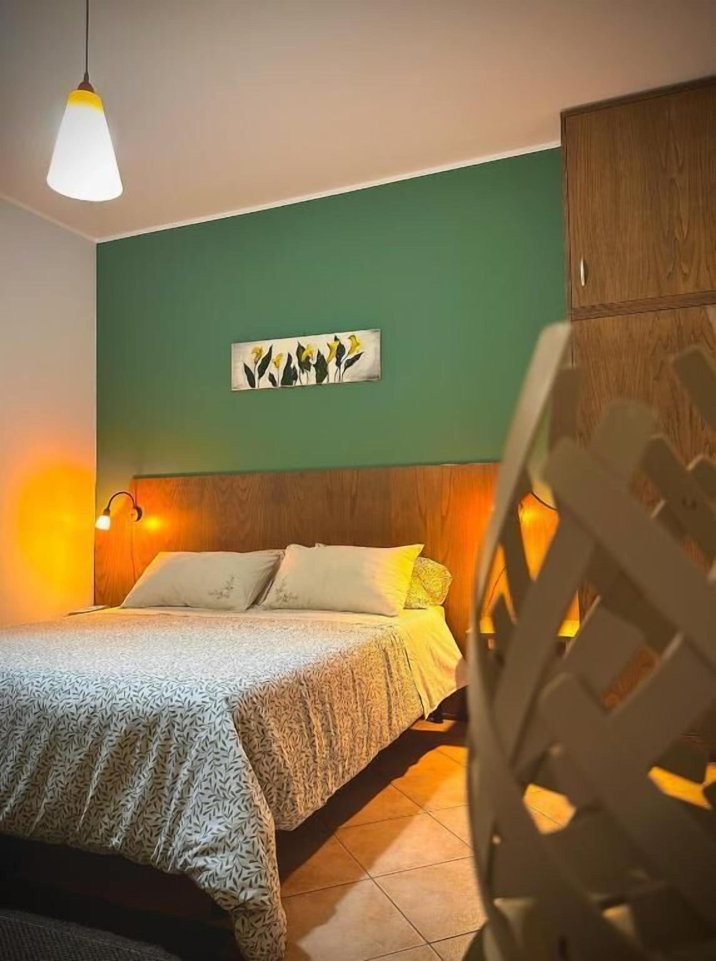 Un dormitorio con una cama, una luz empotrada, un cabecero de madera y una pared verde.