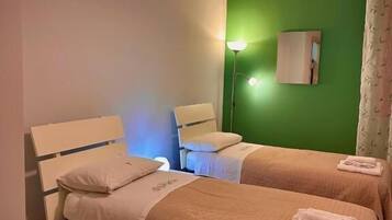 Una camera d'albergo con due letti, una parete verde decorativa, una lampada a sospensione e un comodino.