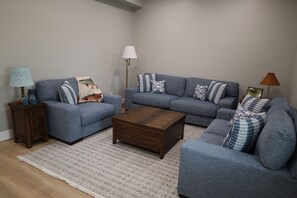 Ein Wohnzimmer mit einem blauen Sofagarnitur, einem Holztisch und einem gemusterten Teppich.