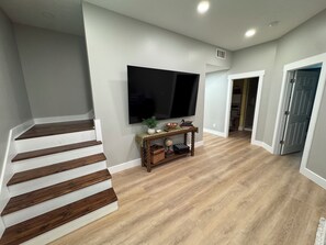 Un salon moderne avec un escalier, un téléviseur à écran plat fixé au mur et une console sur laquelle sont disposés des objets décoratifs.