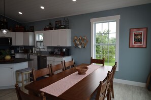 Une cuisine moderne avec des meubles blancs, une table à manger avec des chaises et une grande fenêtre donnant sur un paysage verdoyant.