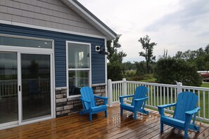 Eine Holzterrasse mit blauen Adirondack-Stühlen, einem weißen Geländer und einem Haus mit blauem Farbanstrich und gemauertem Fundament.