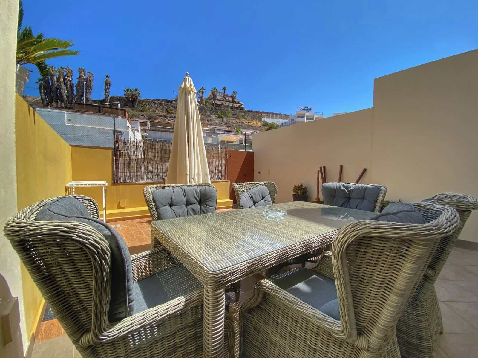 Eine Terrasse mit Korbmöbeln, einem Tisch und einem Sonnenschirm.