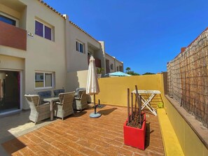 Eine Terrasse im Freien mit Korbmöbeln, einem roten Pflanzgefäß und einer gelben Wand.