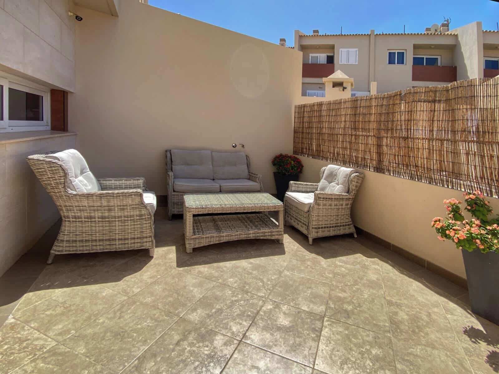 A patio with wicker furniture, a tiled floor, and a bamboo fence.