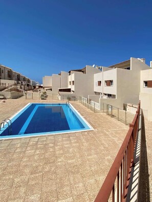 Une piscine dotée d’une terrasse carrelée, entourée de bâtiments modernes avec des balcons.