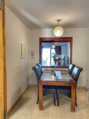 Un coin repas avec une table en bois, quatre chaises, un vase de fleurs, un téléphone et une fenêtre donnant sur un beau paysage.