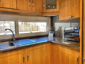 A kitchen with wooden cabinets, a stainless steel sink, and a window with a view of the outside. - Los Corales 1 - Four Bed Townhouse (Arona)