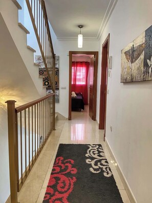 A hallway with a staircase, a patterned rug, and a painting on the wall. - Los Corales 1 - Four Bed Townhouse (Arona)