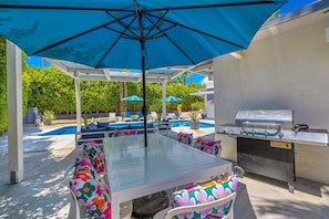 Eine Terrasse im Freien mit Tisch, Stühlen, Grill und Pool.