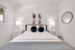 Ein Schlafzimmer mit einem Bett, zwei Nachttischen, einem wandmontierten Spiegel und vier gerahmten Bildern.