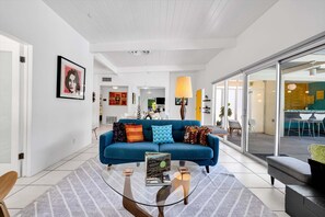 A living room with a blue sofa, a glass coffee table, and a large window. - Experience Authentic Palm Springs Style at Meiselman Palms (Palm Springs)