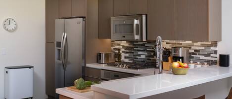 A modern kitchen with stainless steel appliances, a central island, and a clock on the wall.