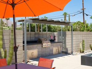 Ein Grillplatz im Freien mit Grill, Sitzgelegenheiten und einer Pergola.