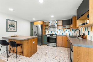 A modern kitchen with a central island, bar stools, a refrigerator, stove, oven, and a backsplash with colorful tiles. - Experience a Fresh Take on Palm Springs Luxury at Solstice Sonora (Palm Springs)