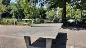 En bänk gjord av betong med en metallyta, placerad i en park med träd och ett belagt underlag.