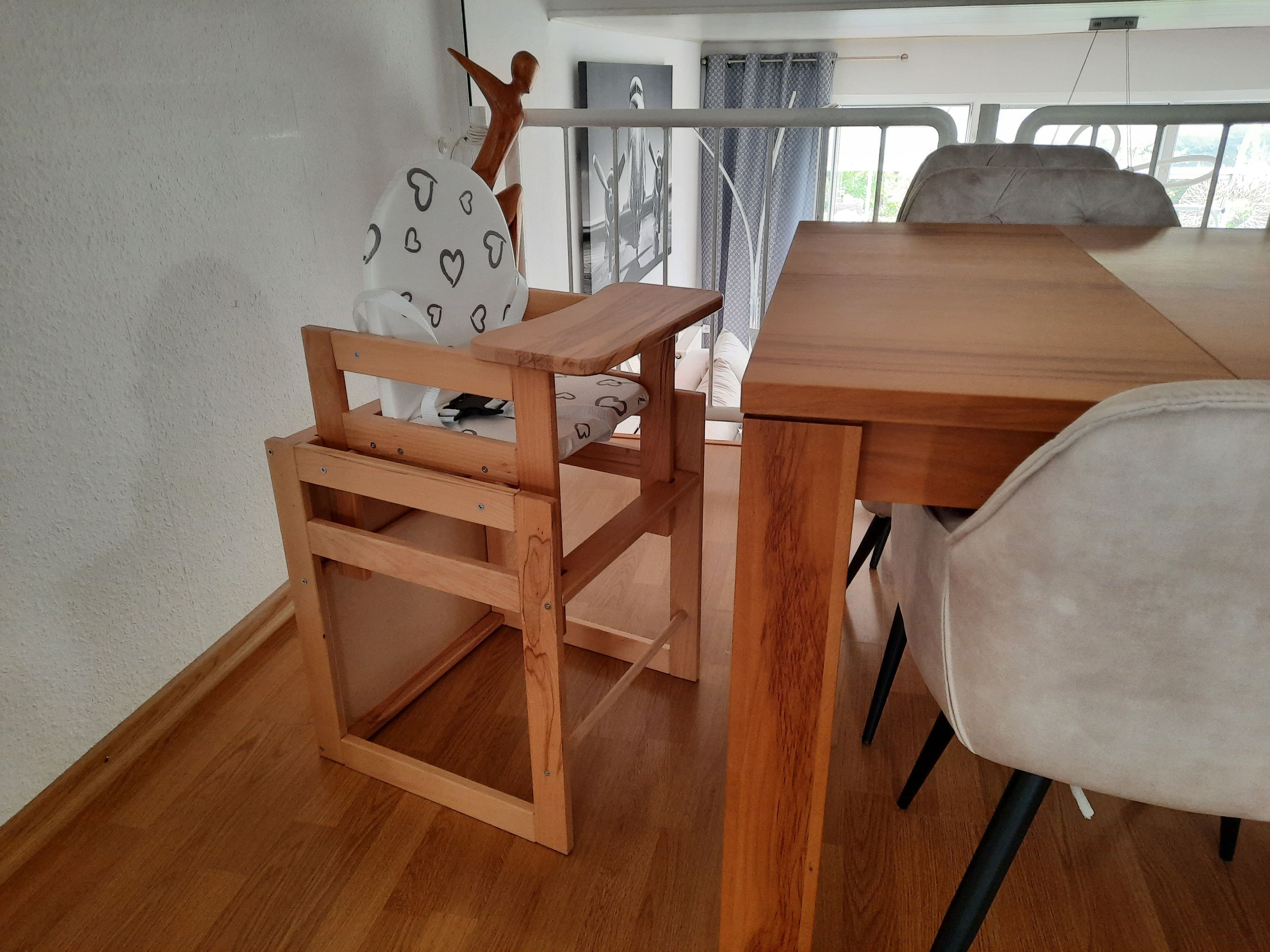 Une table de salle à manger en bois, avec des chaises, un petit tabouret en bois et un coussin blanc orné de motifs en forme de cœur.