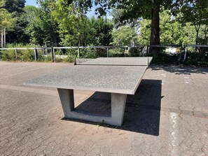 Um banco de concreto com tampo metálico em um parque com árvores e chão calçado.