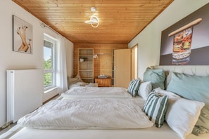 Un dormitorio con una cama grande, techo de madera, radiador, ventana y un cuadro en la pared.