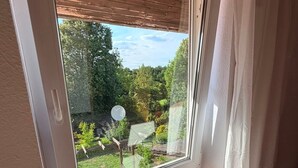 Habitació amb una finestra gran, un sòl de fusta i una taula petita amb un ram de flors.