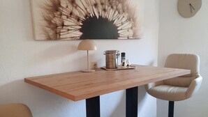 Zona de menjador amb taula de fusta, dues cadires, una làmpada i una peça decorativa a la paret.