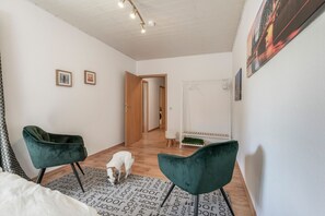 A room with a wooden floor, two green chairs, a white dog, and a door leading to another room. - Holiday Home 'Joanna' with Mountain View, Private Terrace and Wi-Fi (Hennef)
