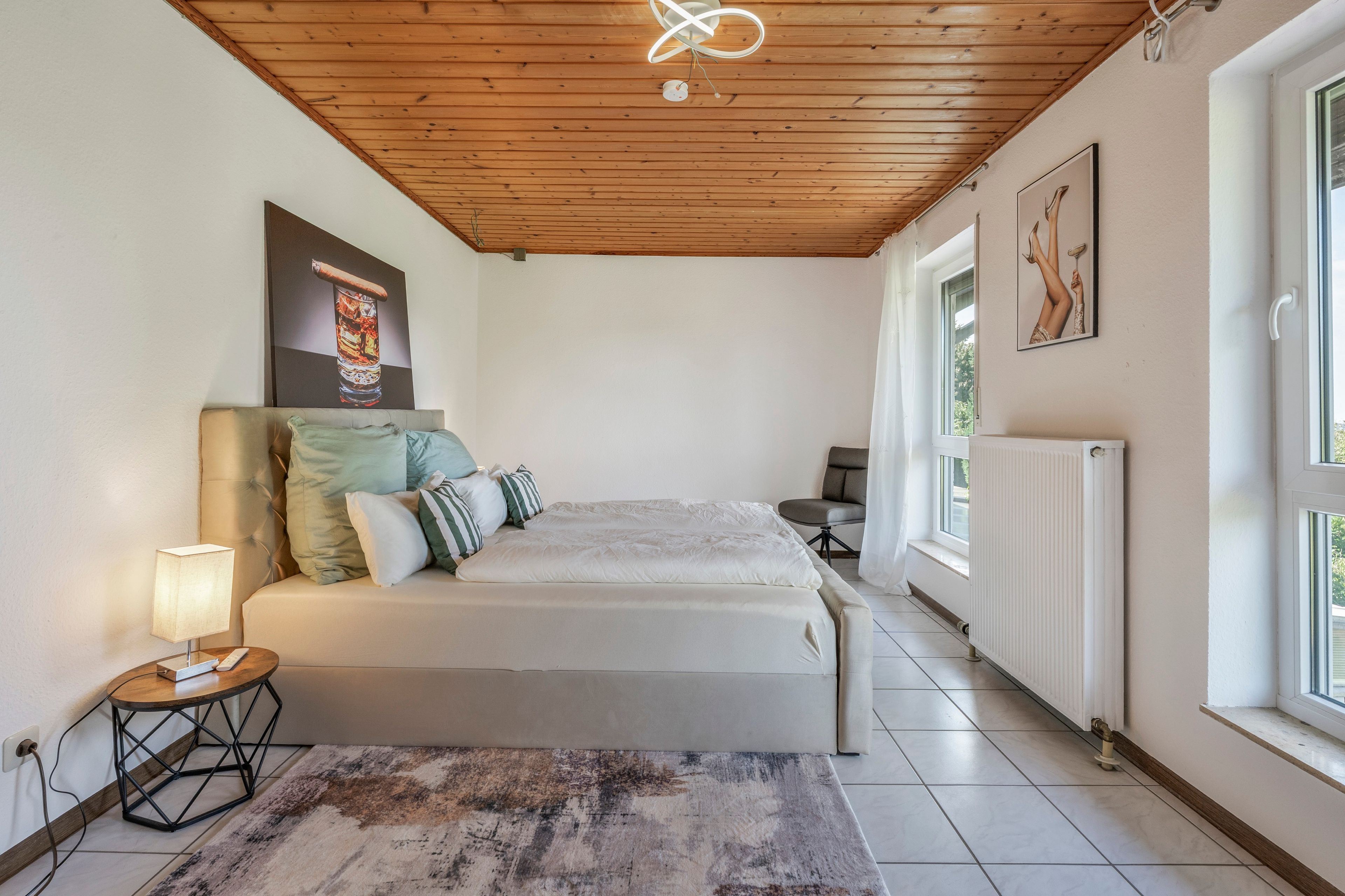 Une chambre à coucher avec un lit, une table de chevet, une lampe, une fenêtre et un radiateur.