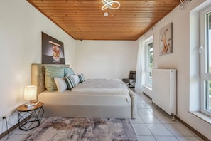 Um quarto com cama, mesa de cabeceira, abajur, janela e radiador.