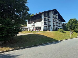 A multi-story hotel with a flat roof, a covered outdoor seating area, and a grassy lawn.