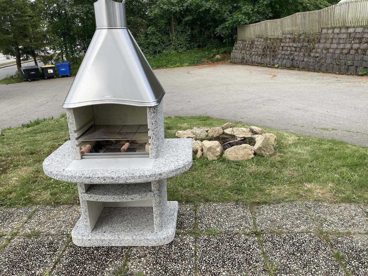 Un four à pizza extérieur en pierre, doté d’une cheminée, entouré d’une zone recouverte de gravier et d’un muret en pierre.