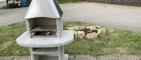 A stone-built outdoor pizza oven with a chimney, surrounded by a gravel area and a stone wall.