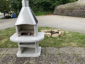 A stone-built outdoor pizza oven with a chimney, surrounded by a gravel area and a stone wall.