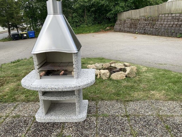 A stone-built outdoor pizza oven with a chimney, surrounded by a gravel area and a stone wall.