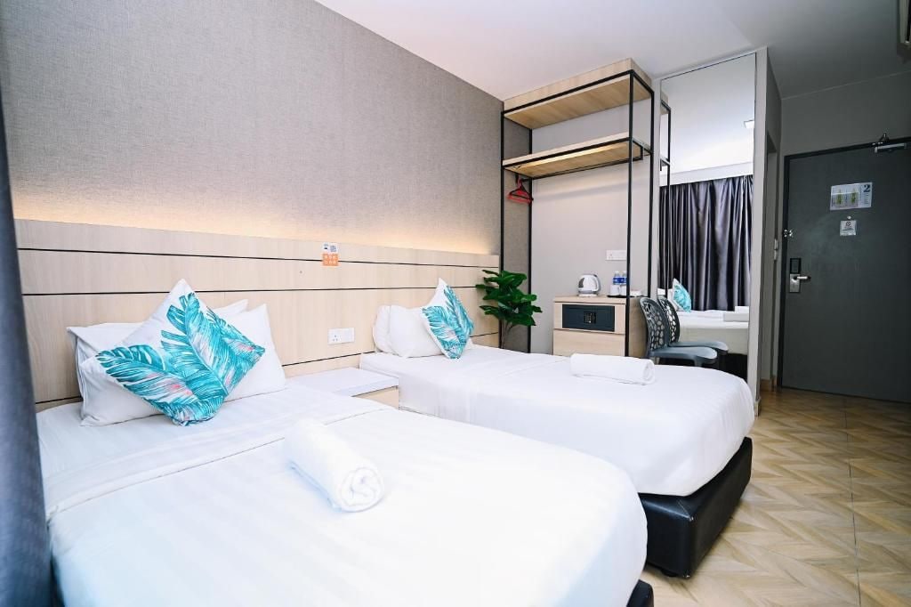 A hotel room with two beds, a small kitchenette, a mirror, and a door.
