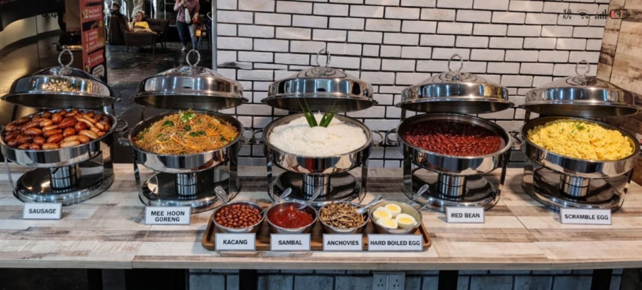 Un bufé con diversos platos, incluyendo salchicha, mee hoon goreng, frijol rojo y huevos revueltos.
