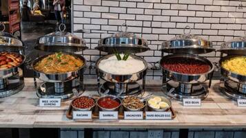 Un bufé con diversos platos, incluyendo salchicha, mee hoon goreng, frijol rojo y huevos revueltos.